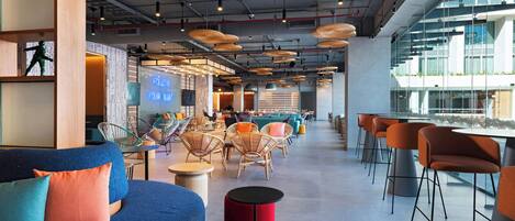 A modern lounge area with seating arrangements, a bar area, and a visible outdoor view through large windows.