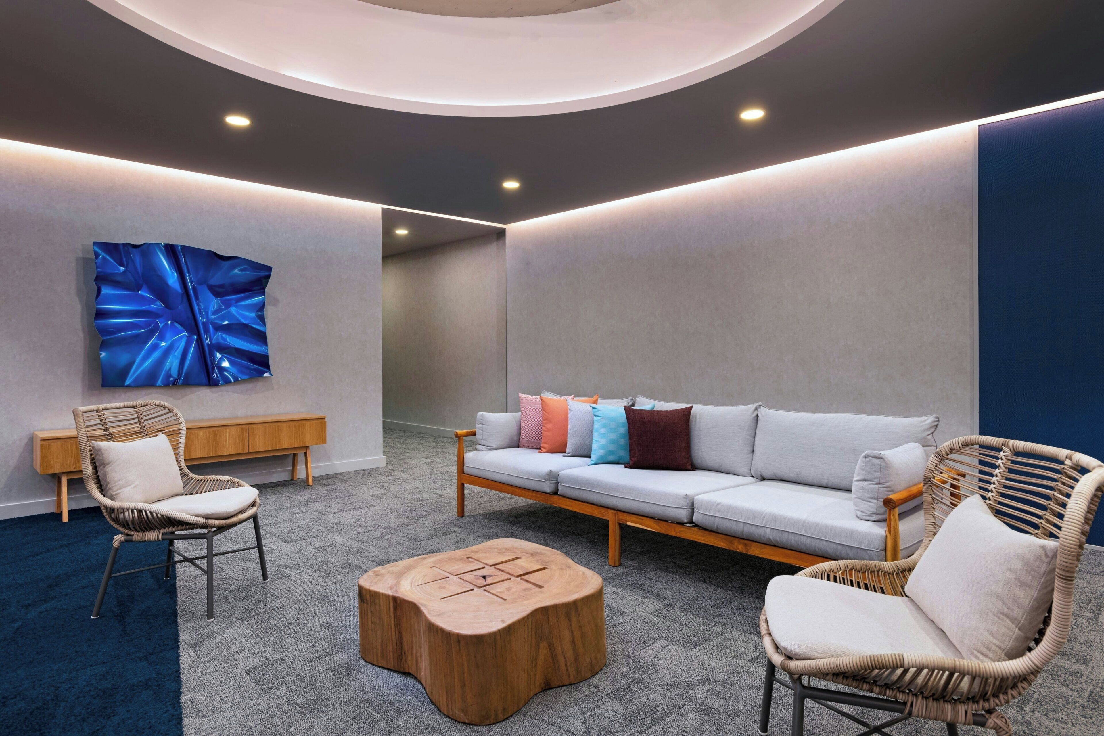 A modern lounge area with a sofa, two wicker chairs, a wooden coffee table, and a large abstract painting on the wall.
