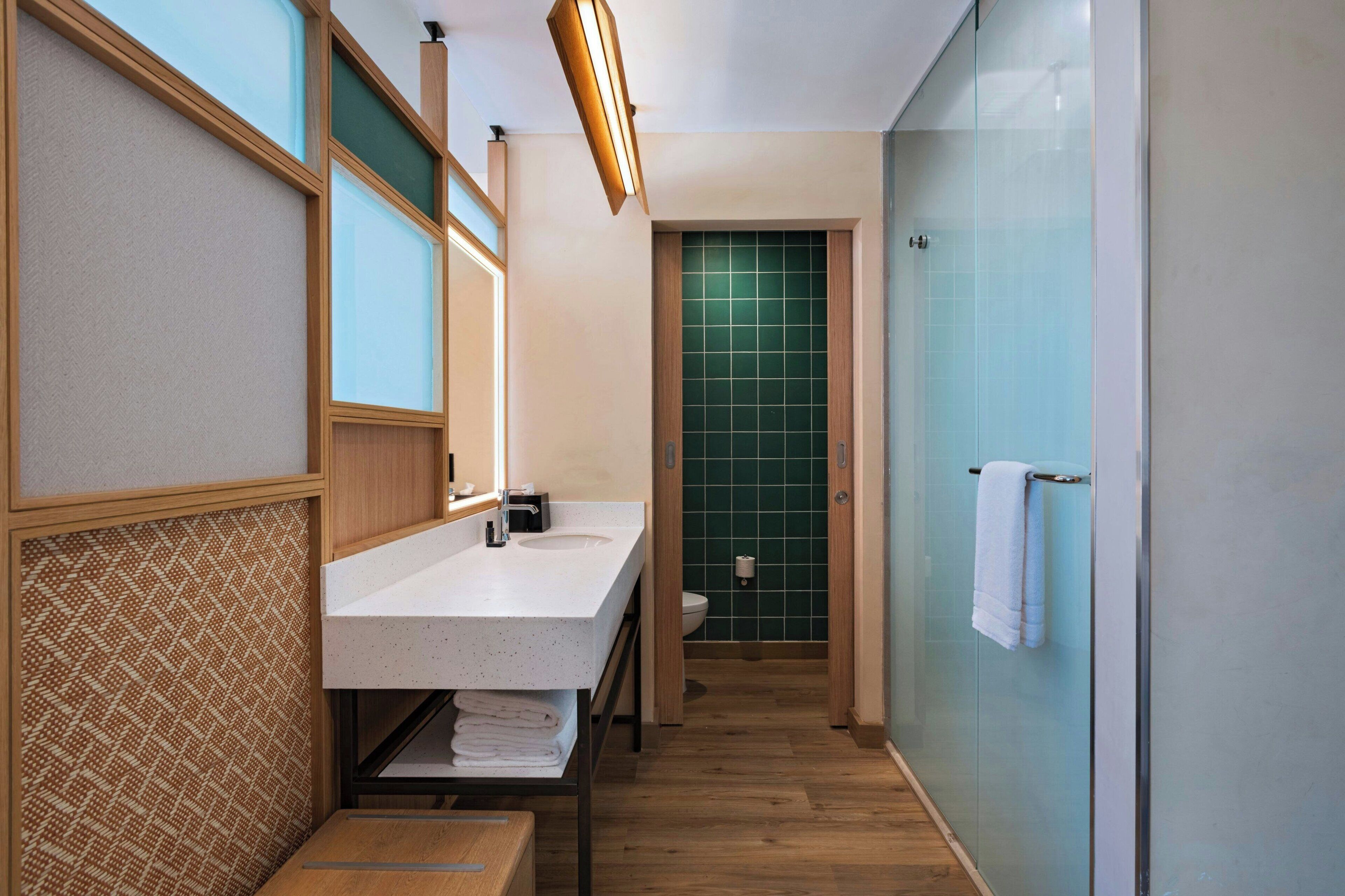 Ein modernes Badezimmer mit einem Holzbadschrank, einer Glasdusche und einer grünen Wandfliesen.