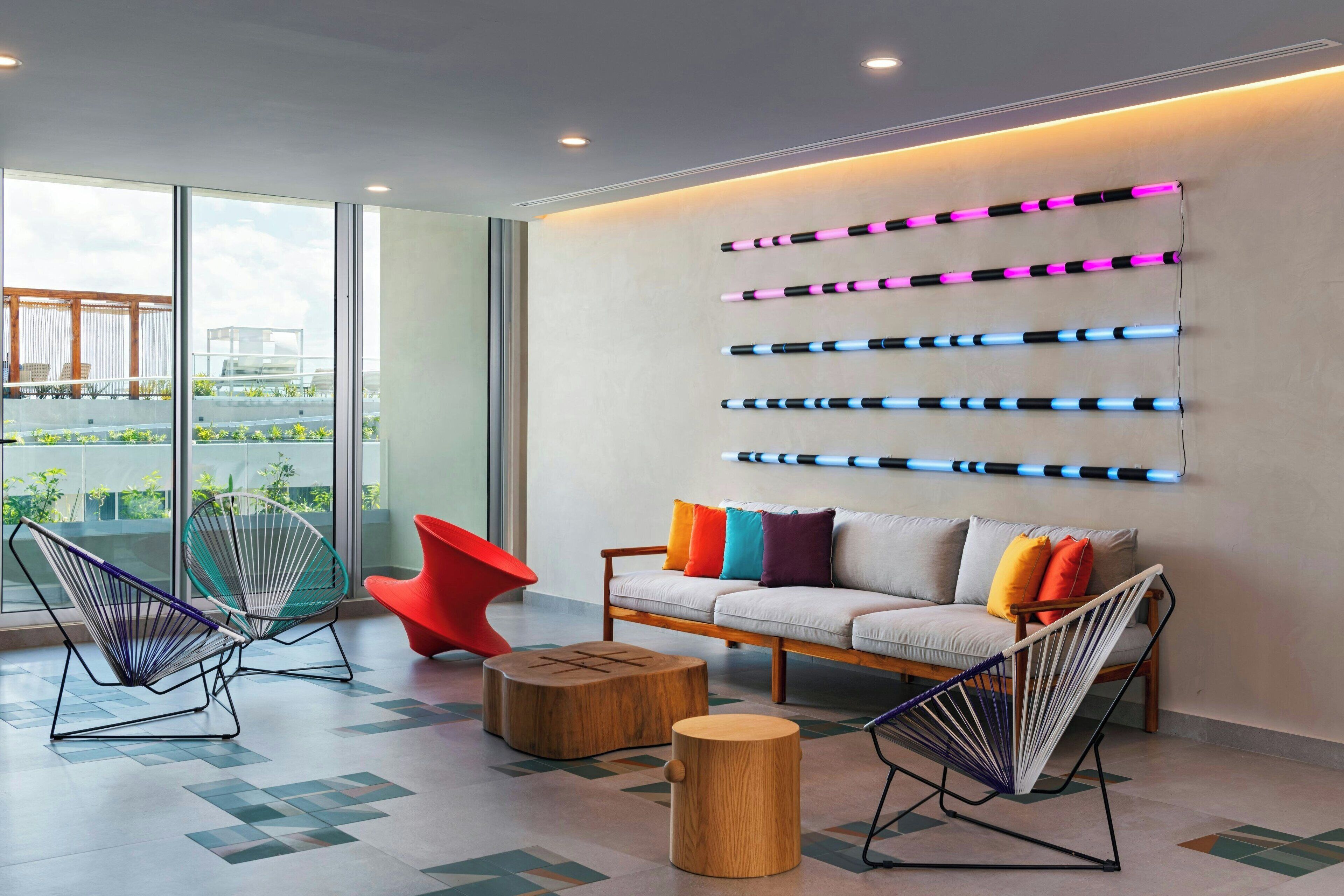A modern lounge with a sofa, colorful cushions, and unique chairs.