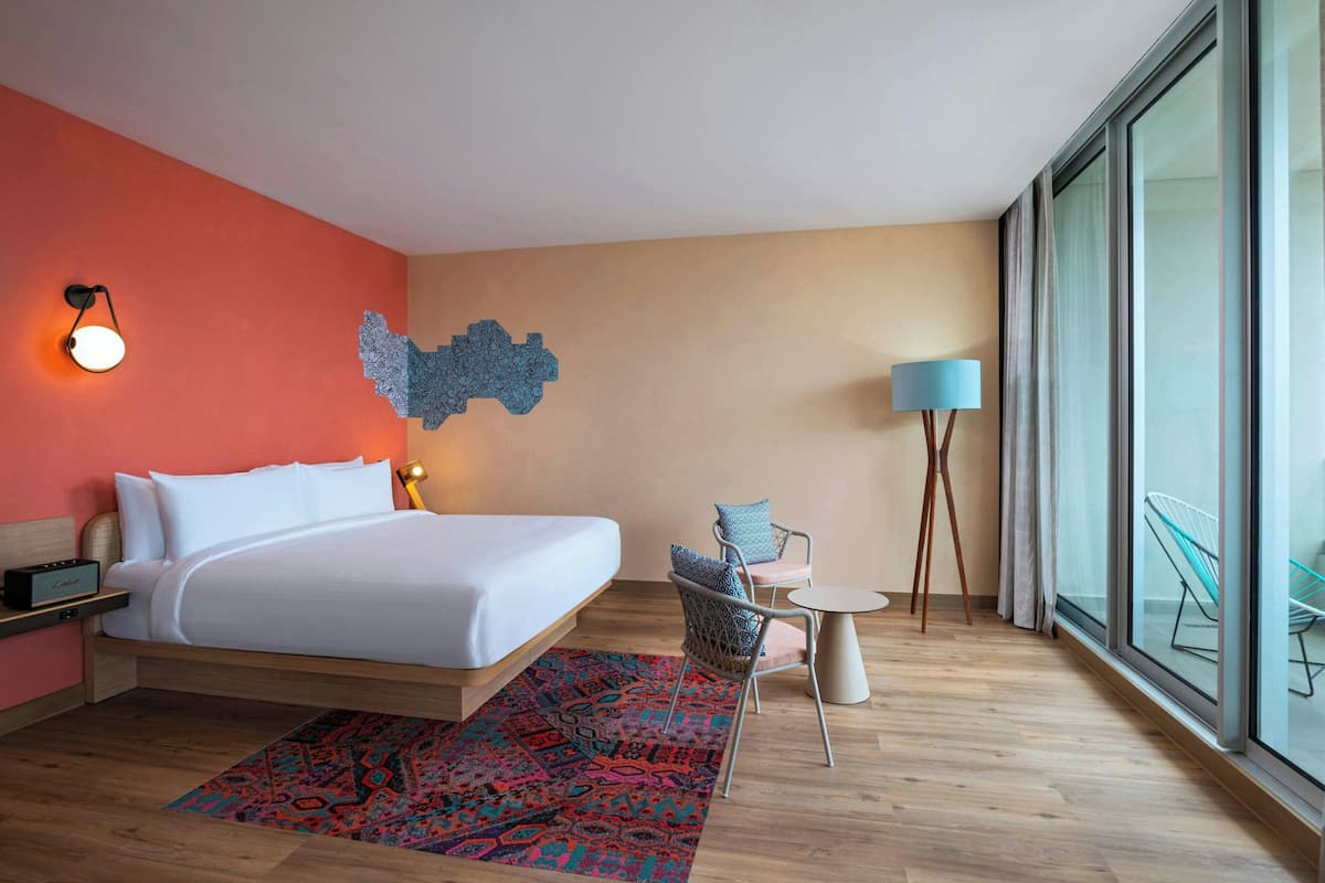 Une chambre d’hôtel moderne, dotée d’un grand lit, d’une petite table, d’une chaise et offrant une vue sur l’extérieur grâce à de grandes fenêtres.