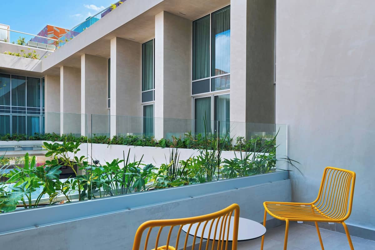 Un bâtiment moderne doté d’un balcon, de deux chaises jaunes et offrant une vue sur la rue.