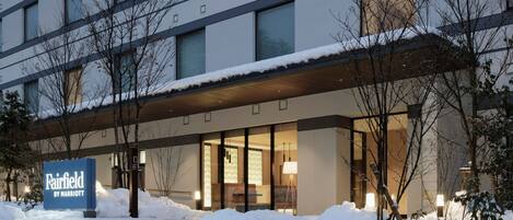 A hotel entrance with a snow-covered ground, a sign reading "Fairfield by Marriott," and a modern building facade with large windows.