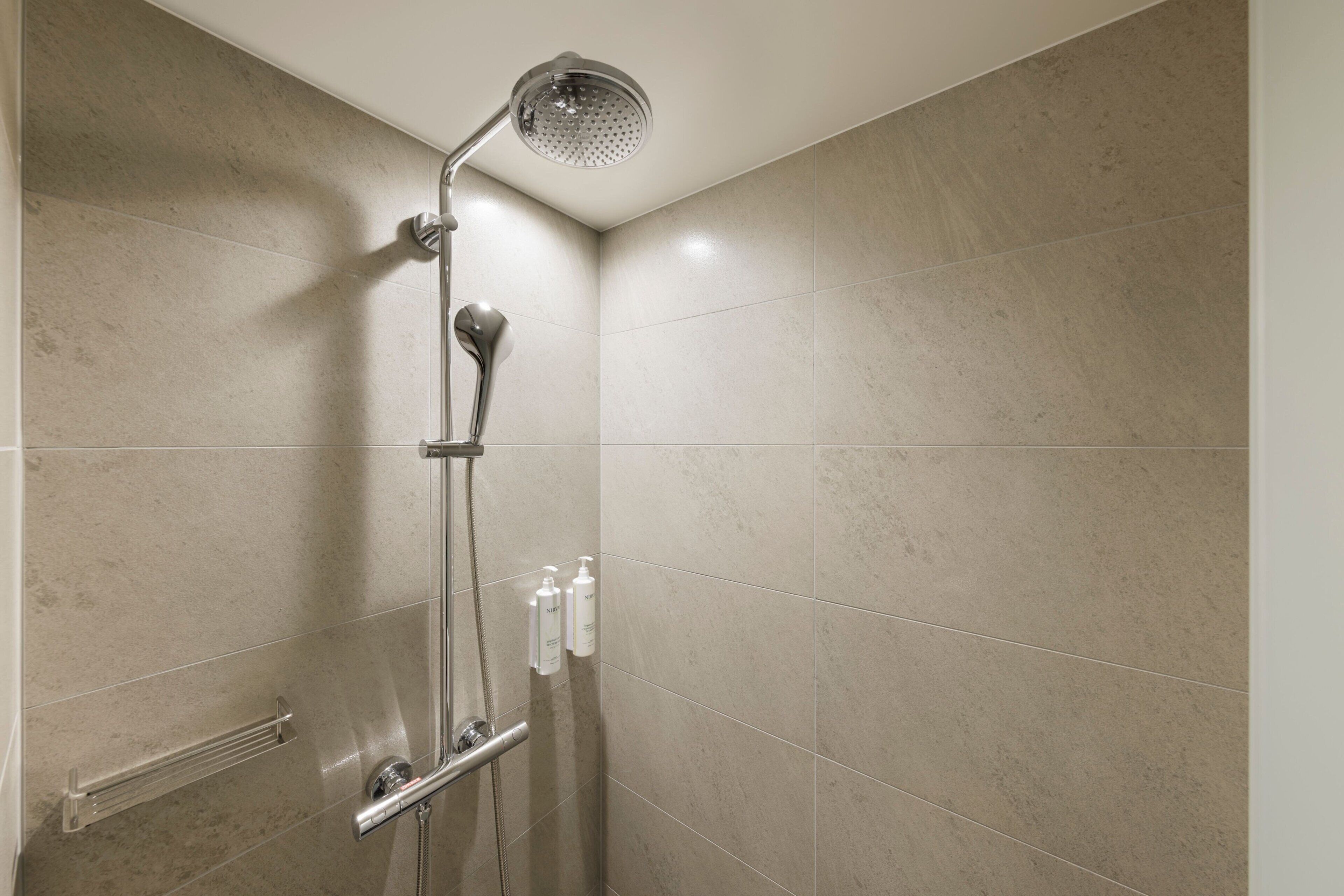 A modern shower with a handheld showerhead and a handheld rain shower attachment.