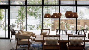 Un moderno comedor con una mesa grande y sillas, ventanas amplias con vistas a la vegetación exterior, y lámparas de mimbre colgantes.