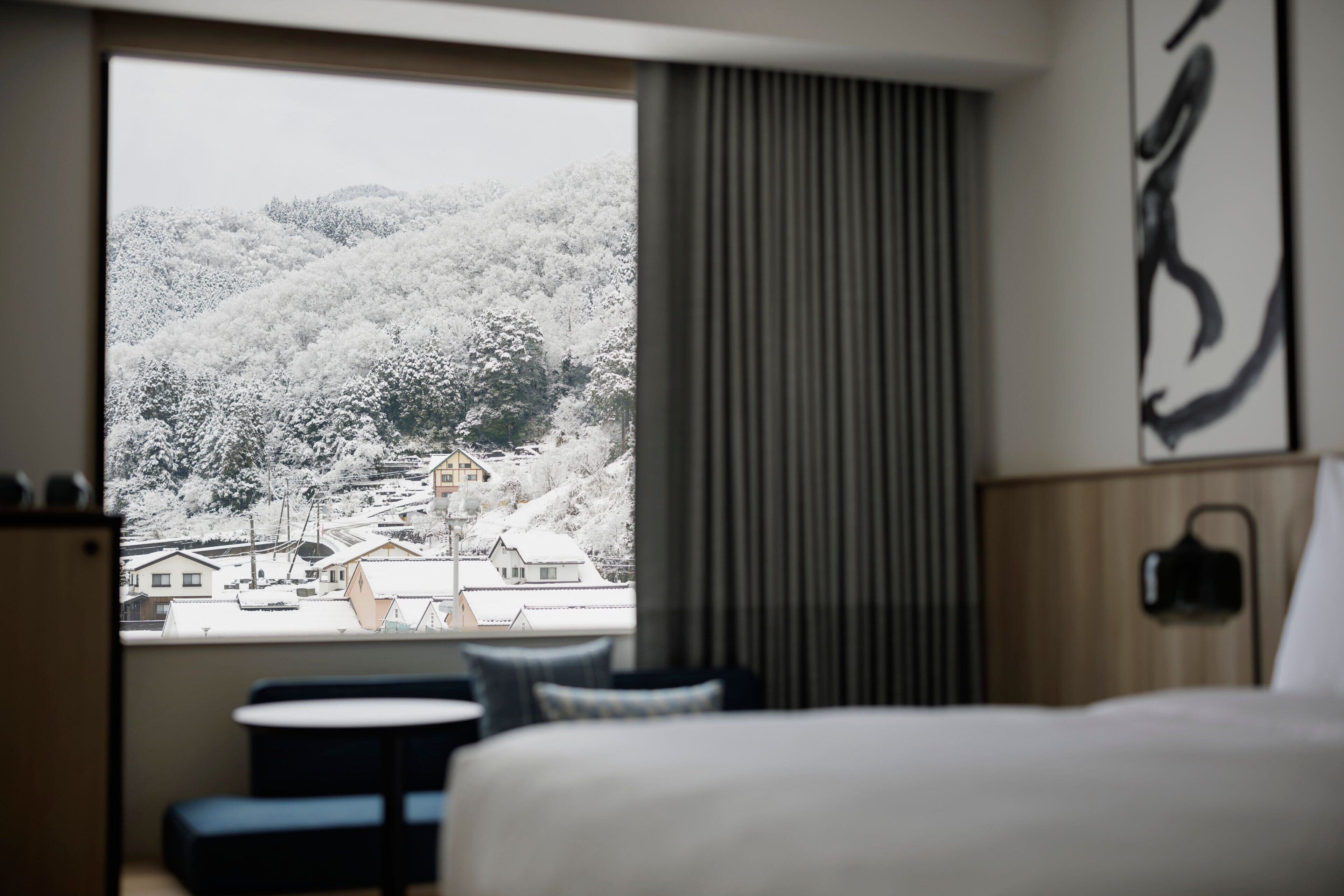 A hotel room with a large window offering a view of a snow-covered landscape and buildings.