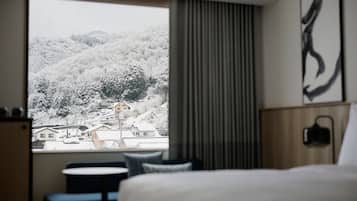 A hotel room with a large window offering a view of a snow-covered landscape and buildings.