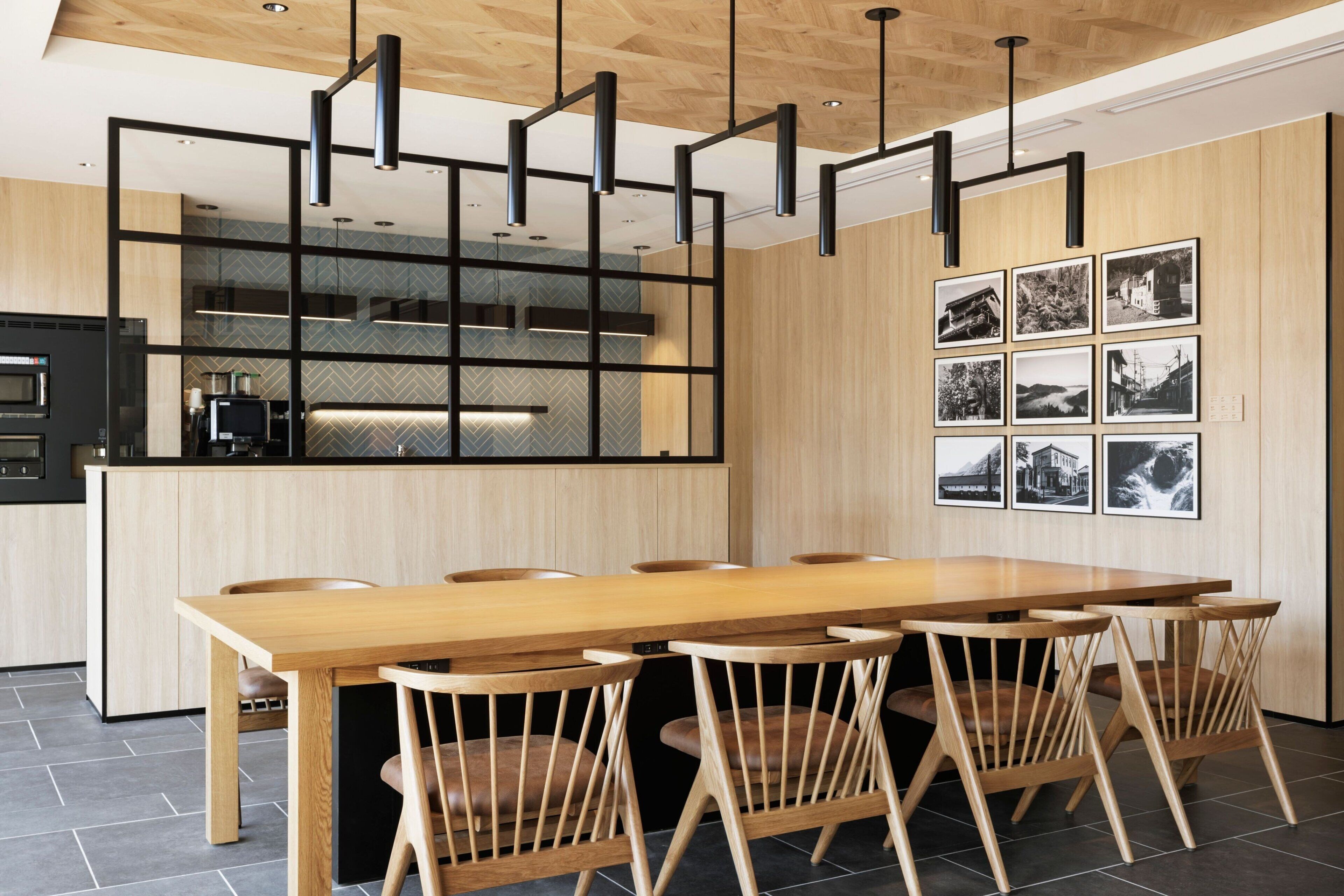 A modern kitchen with a wooden dining table and chairs, a built-in oven, and a black-framed hanging light fixture.