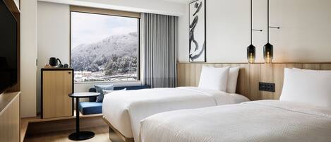 Habitación de hotel moderna con dos camas, una mesita, televisión y un amplio ventanal con vistas a un paisaje nevado.