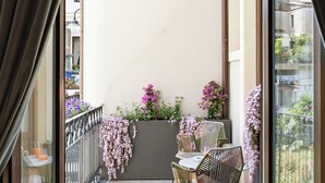 A balcony with wicker chairs and a table, a railing, and potted plants.