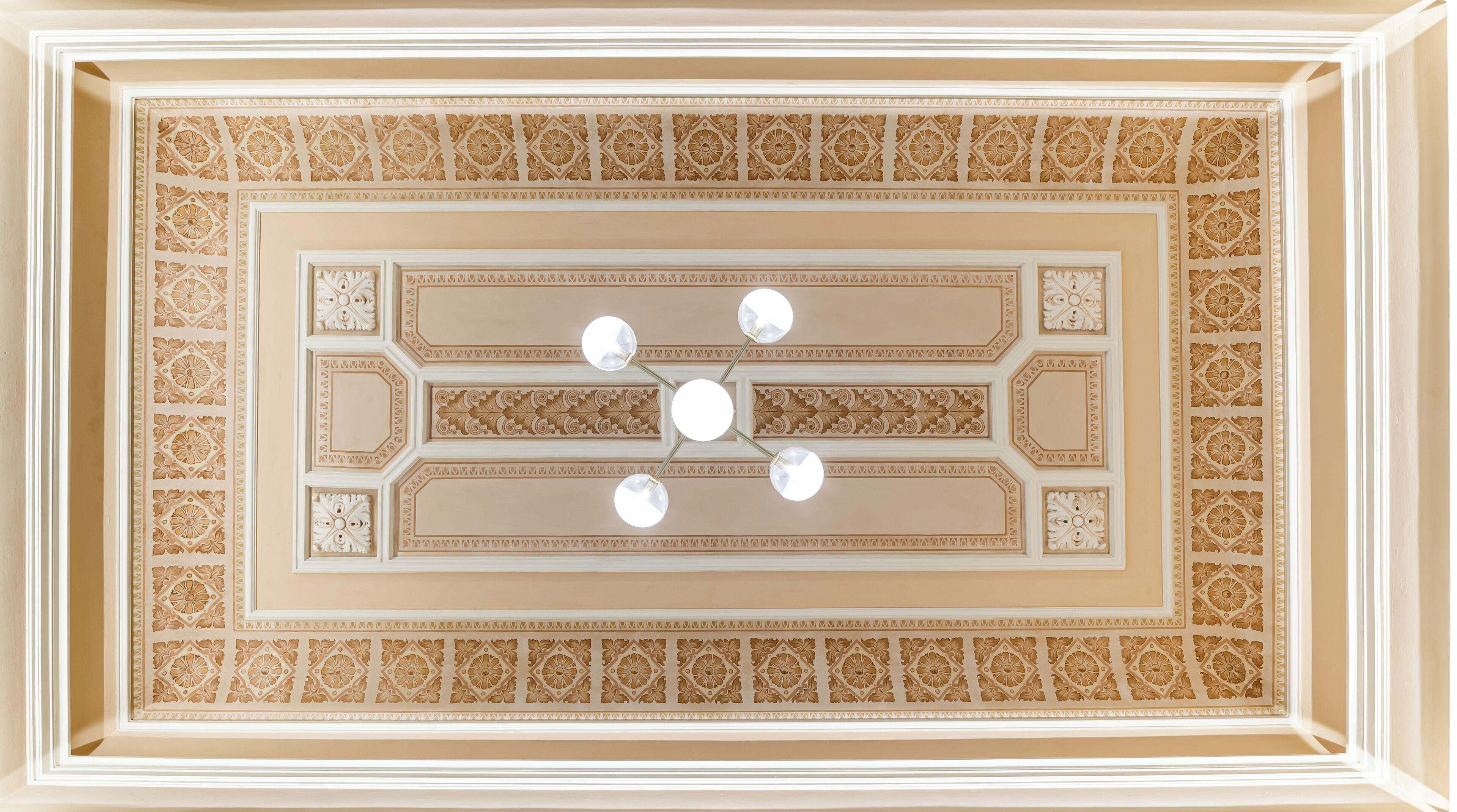 A ceiling with intricate geometric patterns and a central chandelier.