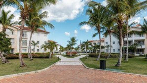 A pathway leading to a building complex with palm trees and a clear sky.