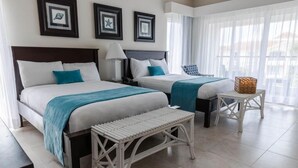 A hotel room with two beds, a bench, a small table, and a chair.