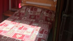 Een eenpersoonsbed met een houten hoofdbord, een quilt met een lappendekenmotief, en een rood gordijn.