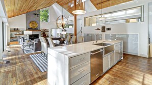 Een moderne keuken met een groot eiland, roestvrijstalen apparatuur en een houten plafond.