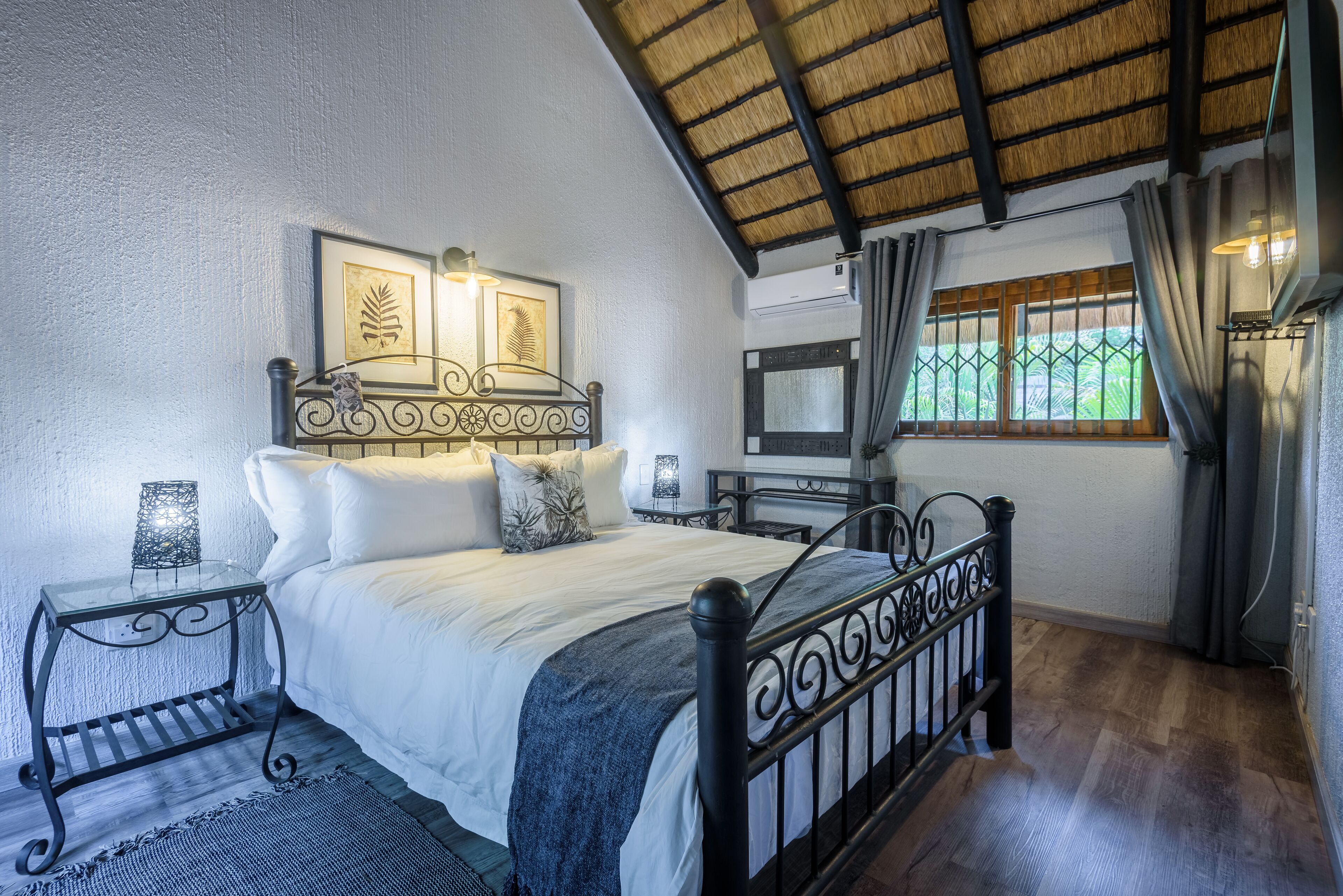 Un dormitorio con cama, mesitas de noche, televisión y ventana con cortinas.