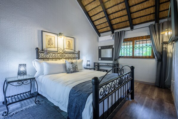 Un dormitorio con cama, mesitas de noche, televisión y ventana con cortinas.