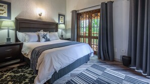 Een slaapkamer met een groot bed, twee nachtkastjes met lampen, een plafondventilator, een kamerbreed tapijt en uitzicht op de omgeving door een deur met gordijnen.