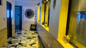 Un pasillo con suelo de mármol, un banco y un espejo decorativo en la pared.