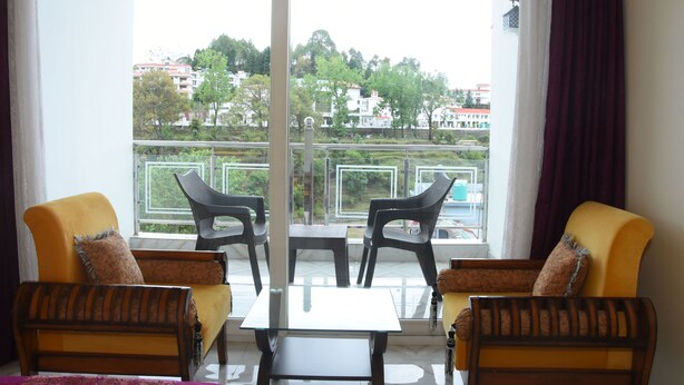 Un balcón con dos sillones amarillos y una mesita, con vista a una zona residencial con árboles y edificios.