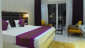 Habitación de hotel con una cama grande, un escritorio, dos sillas y un balcón con cortinas.