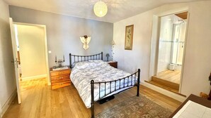 Une chambre à coucher comprenant un lit, une table de chevet, une lampe et donnant sur un espace douche.
