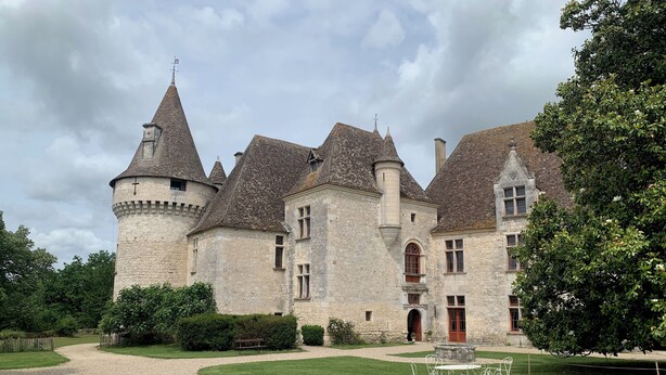 Un château historique en pierre, doté de nombreuses tours et d’une cour intérieure avec un chemin de gravier et une table entourée de chaises.
