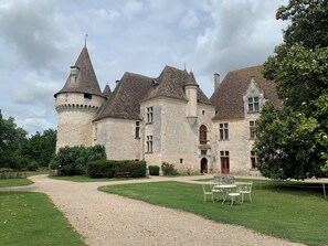 Un château historique en pierre, doté de nombreuses tours et d’une cour intérieure avec un chemin de gravier et une table entourée de chaises.