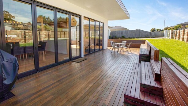 A modern patio with wooden flooring, glass doors, and a seating area with chairs and a table.