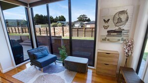 A modern living room with a sofa, a coffee table, and a small plant. There is a large window providing a view of the outdoors.