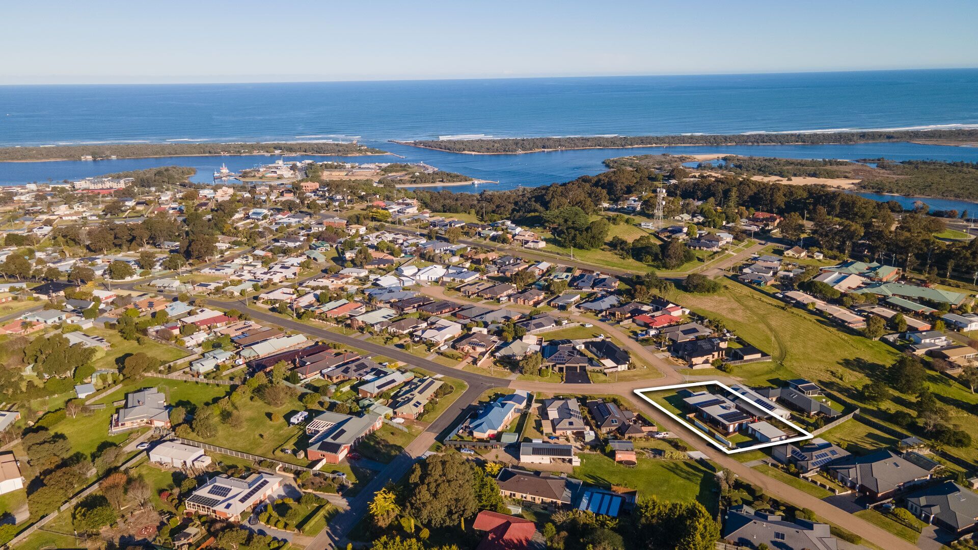 An aerial view of a residential area with houses, roads, and a large body of water in the background.