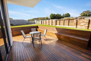 An outdoor patio with a wooden deck, a round table with four chairs, and a built-in bench.