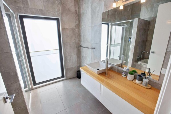 Un baño moderno con un espejo grande, un tocador de madera y una cabina de ducha de vidrio.