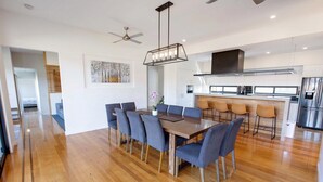 A modern kitchen with a central island, a dining area with a wooden table and chairs, and a ceiling fan.