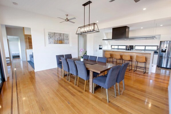 Una cocina moderna con una isla central, un comedor con mesa y sillas de madera, y un ventilador de techo.
