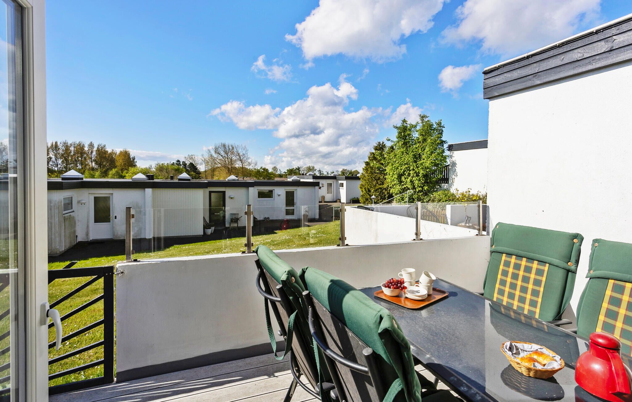 A balcony with a table set for dining, a chair, and a view of mobile homes in the background.