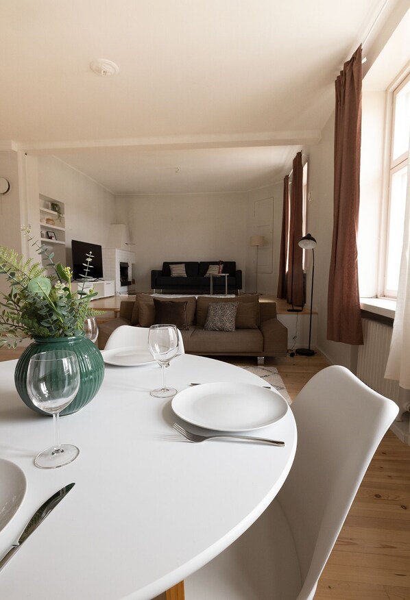 A dining area with a round table, white plates, and a wine glass. There is a green vase with plants on the table.