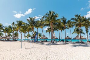 A beach with palm trees, thatched umbrellas, and lounge chairs.