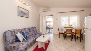 A living room with a sofa, a dining table with chairs, a white coffee table, and a kitchen area with a refrigerator. - Apartment Steindl (Vir)