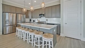 Una cocina moderna con una isla central, electrodomésticos de acero inoxidable e iluminación colgante.