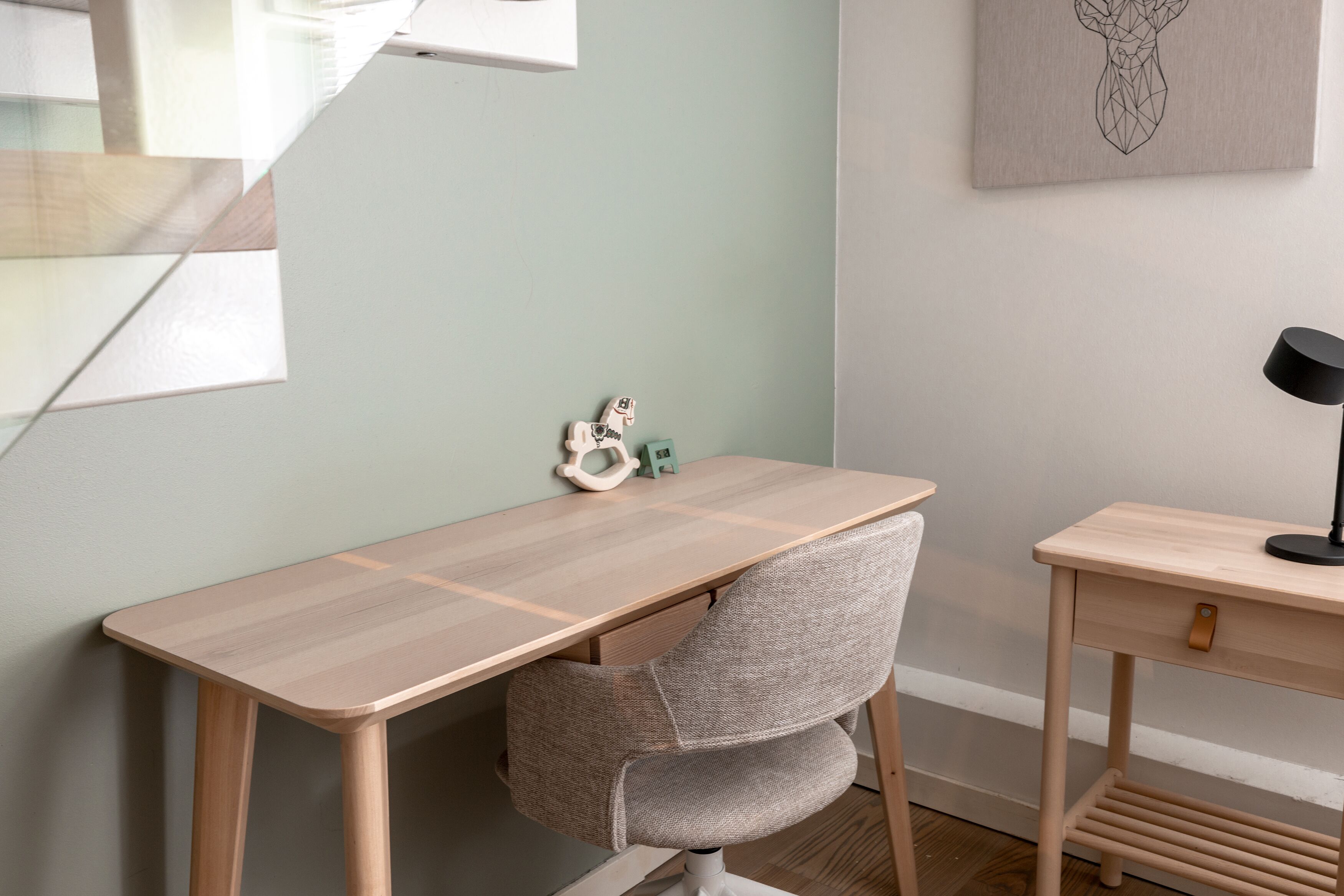 A minimalist office setup with a wooden desk, a grey chair, and a small side table with a lamp.