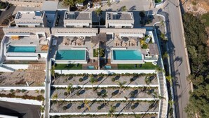 Une vue aérienne d’un complexe hôtelier doté de plusieurs piscines, d’un espace paysager central agrémenté de palmiers et d’une route adjacente à la propriété.