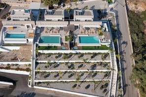 Une vue aérienne d’un complexe hôtelier doté de plusieurs piscines, d’un espace paysager central agrémenté de palmiers et d’une route adjacente à la propriété.