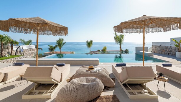 Un espace aménagé au bord de la piscine, avec des chaises longues, une grande piscine et une vue sur la mer.