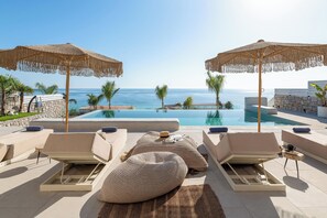 Un área junto a la piscina con sillones reclinables, una piscina grande y vistas al mar.