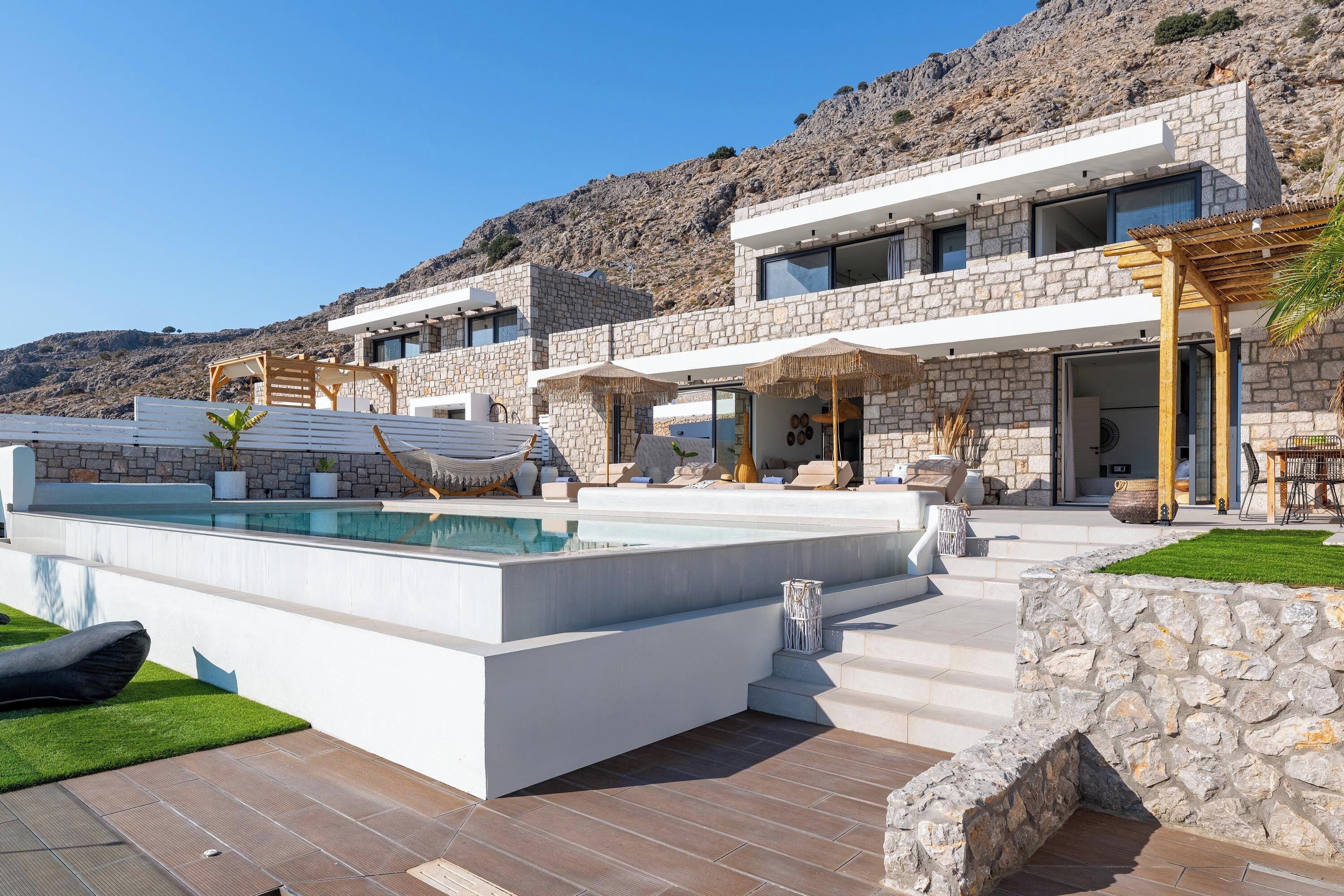 En modern villa med en swimmingpool, utomhusmöbler och en fasad av sten.