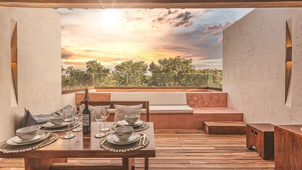 A dining area with a table set for two, a bench, and a view of trees and sky. - Entorno Villas  (Tulum)
