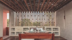 A dining area with a wooden table set for two, a bench, and a view through a bamboo screen. - Entorno Villas  (Tulum)