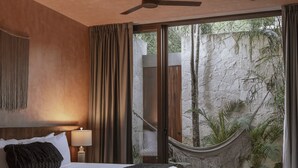 A modern bedroom with a large bed, a ceiling fan, and a view of a natural landscape through large windows. - Entorno Villas  (Tulum)