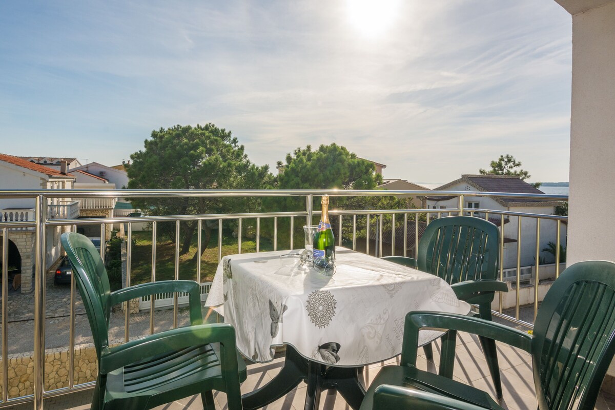 A balcony with a table set for two, a bottle of champagne, and a view of the sea.